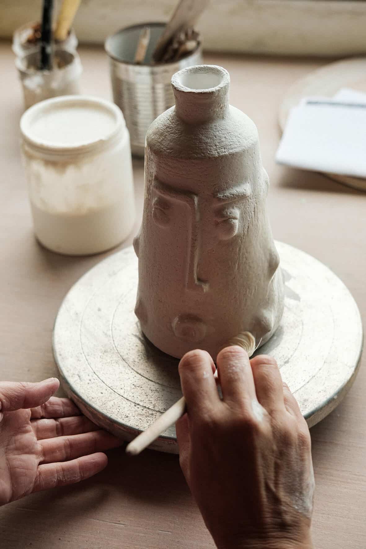 Mãos da ceramista moldam as formas da peça.