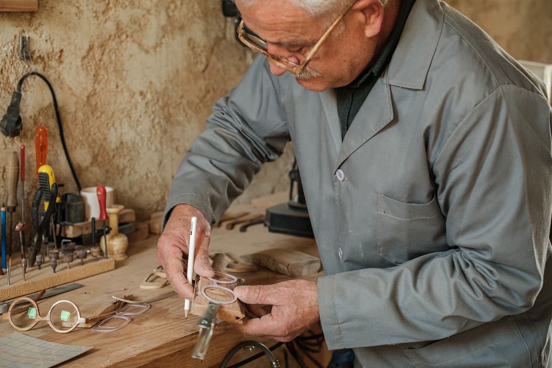 Amâncio traça forma dos óculos com lápis num pedaço de madeira a partir do molde.
