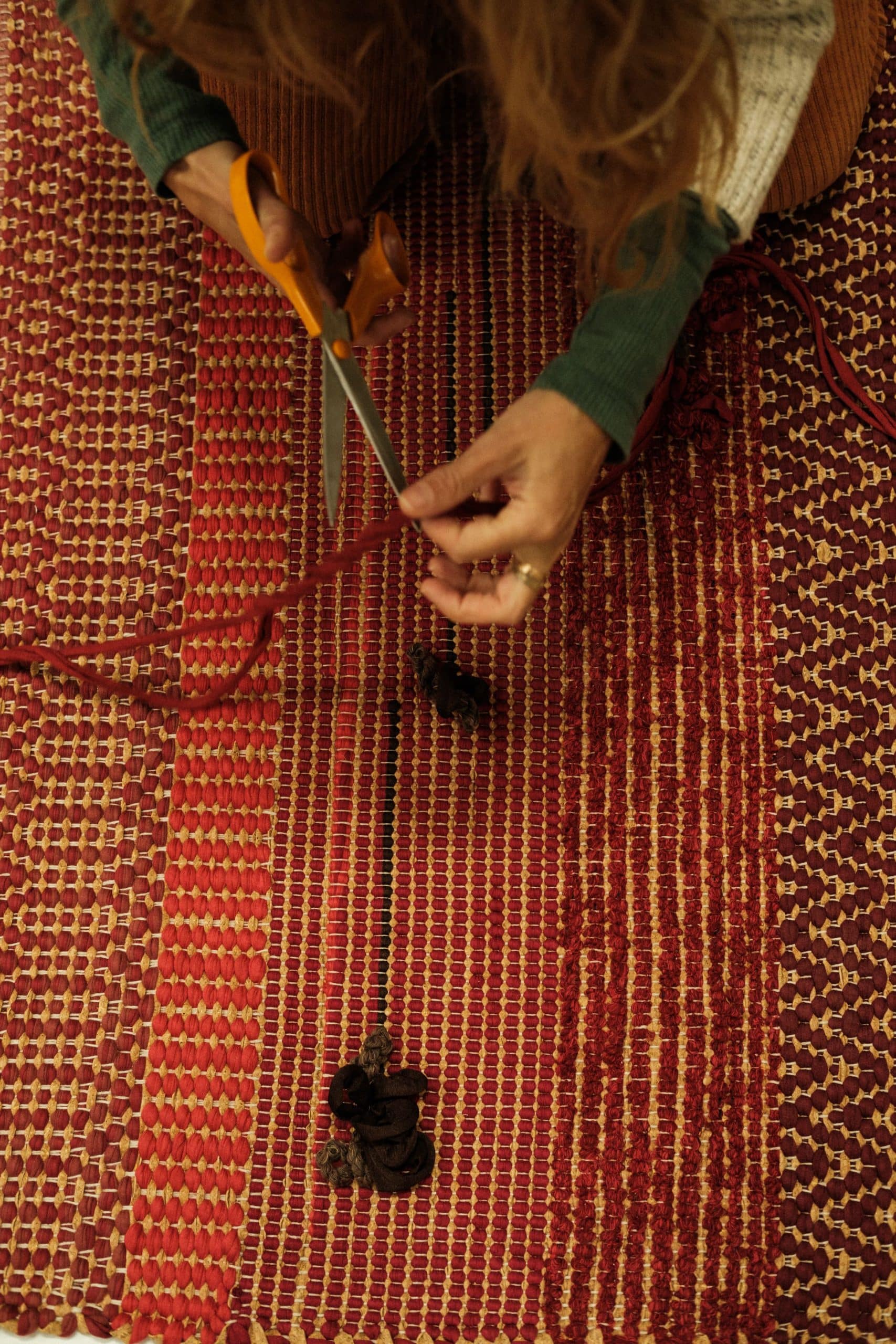 Sentada no chão, Susana trabalha sobre um tapete, cortando um pedaço de linha com a tesoura.
