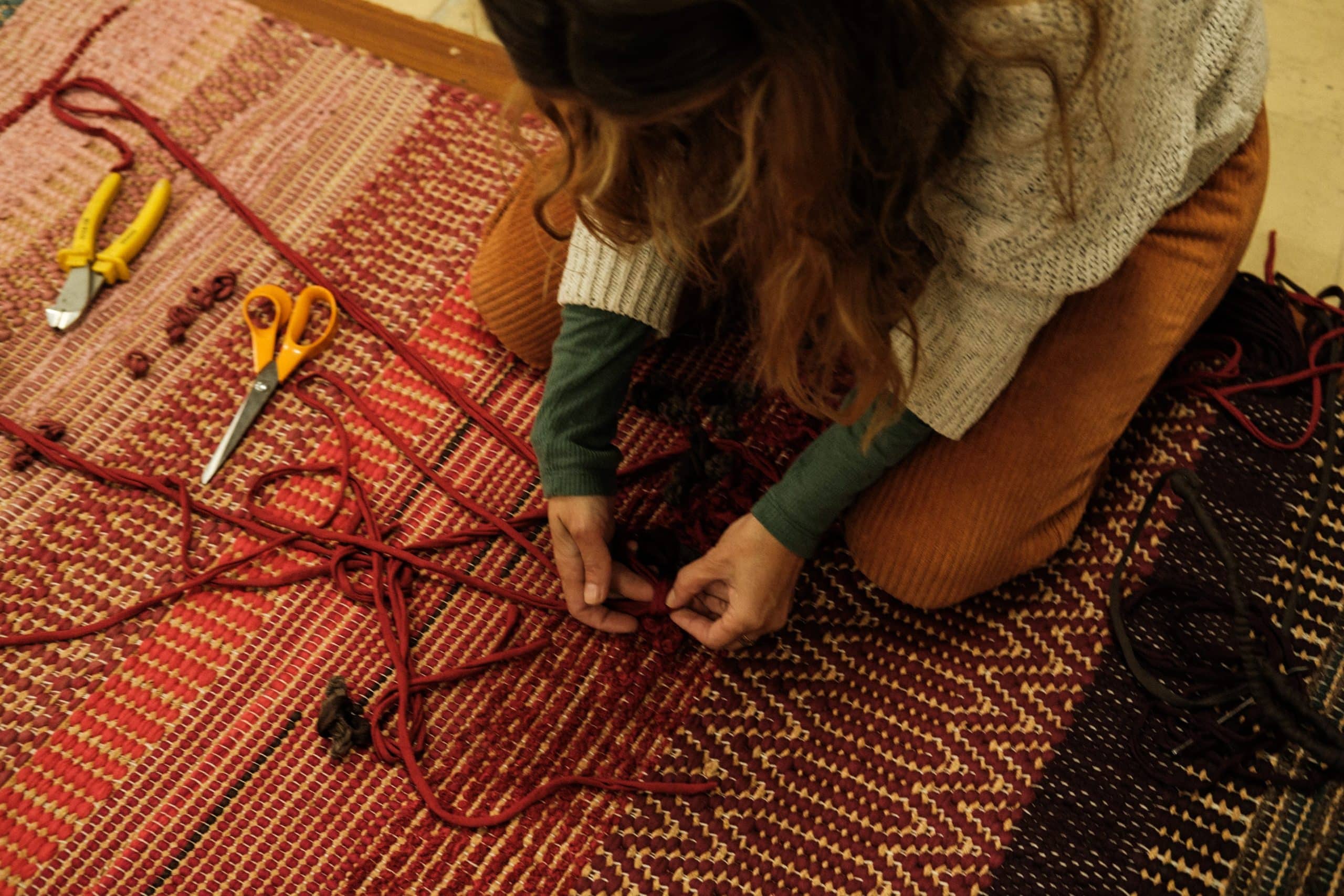 Sentada no chão, Susana trabalha com as suas duas mãos num tapete.