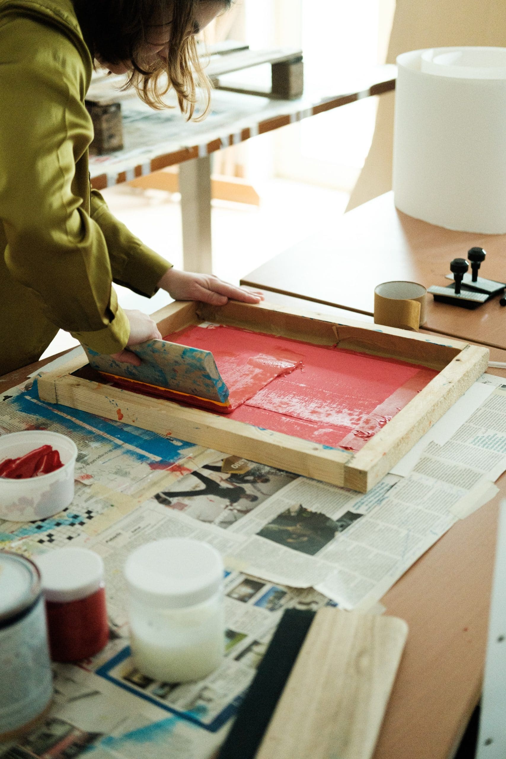 Artista aplica a tinta vermelha na placa de serigrafia com raclete.