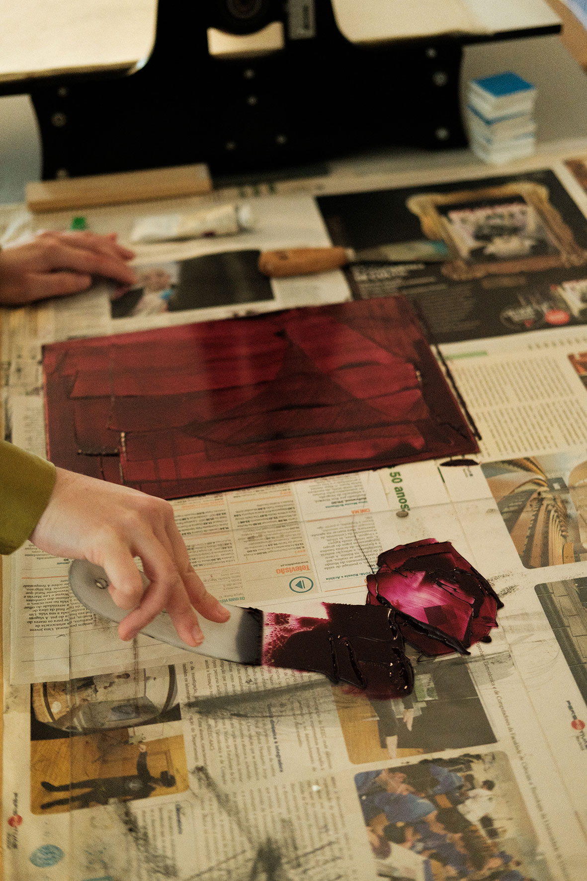 Artista passa tinta numa chapa para gravura com o auxilio de uma espátula.