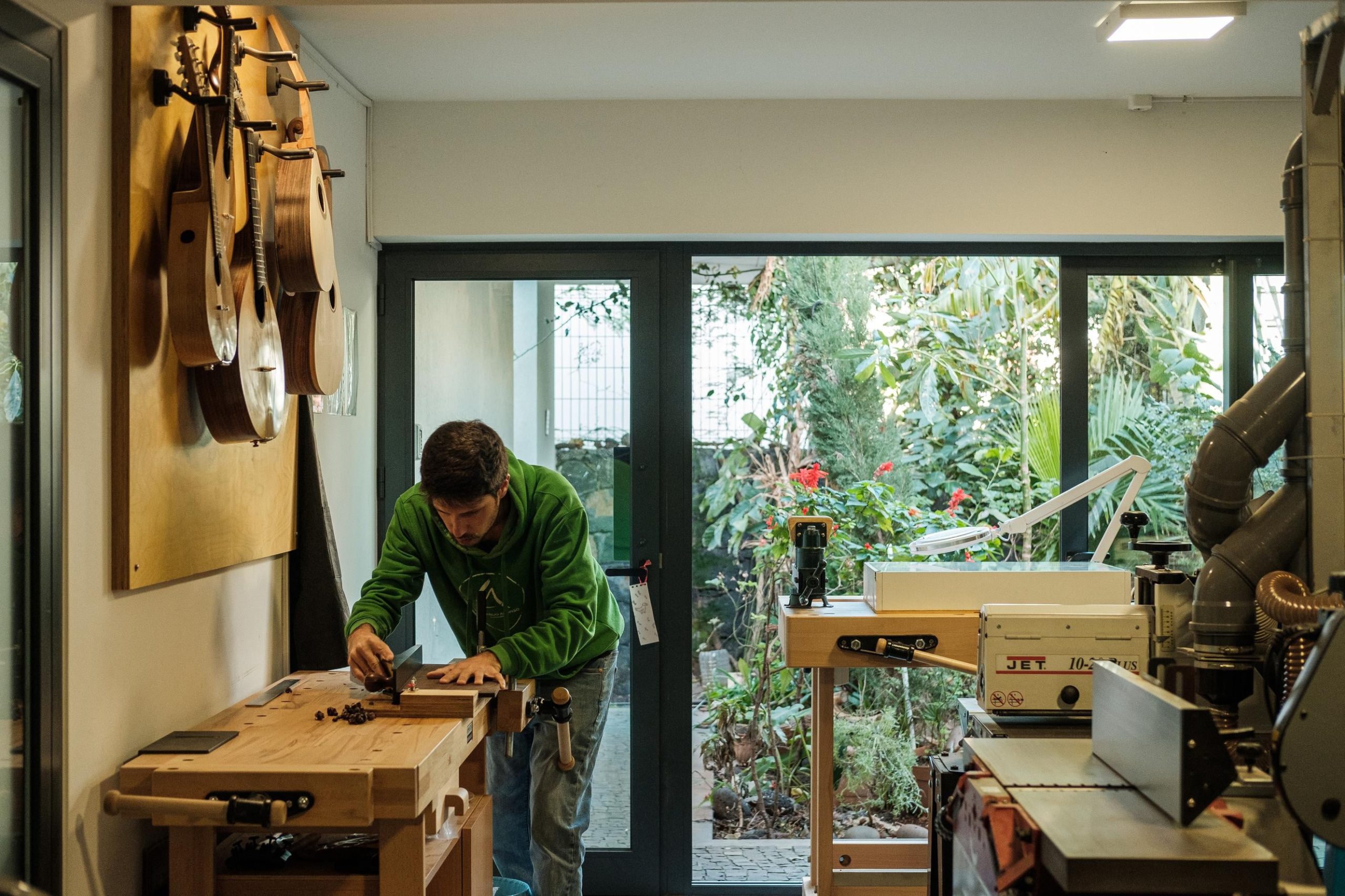Artista Leonardo Afonso a trabalhar na sua oficina. Guitarras penduradas na parede do lado esquerdo e maquinaria do lado direito
