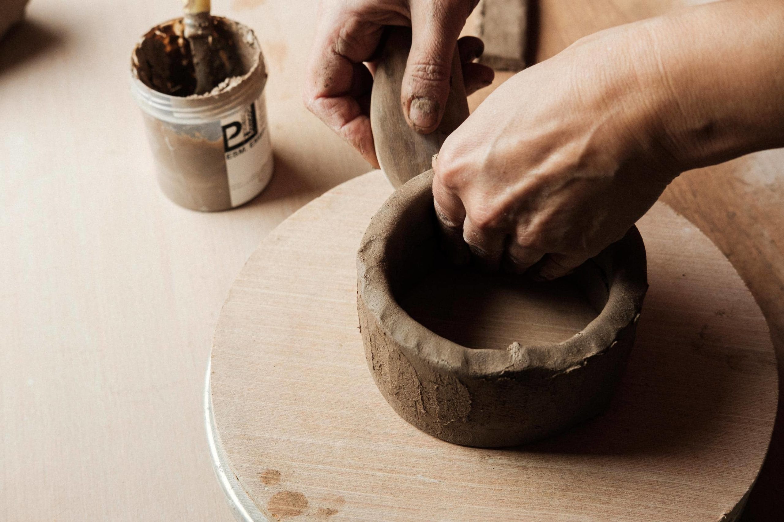 Mãos de ceramista moldam peça de barro.