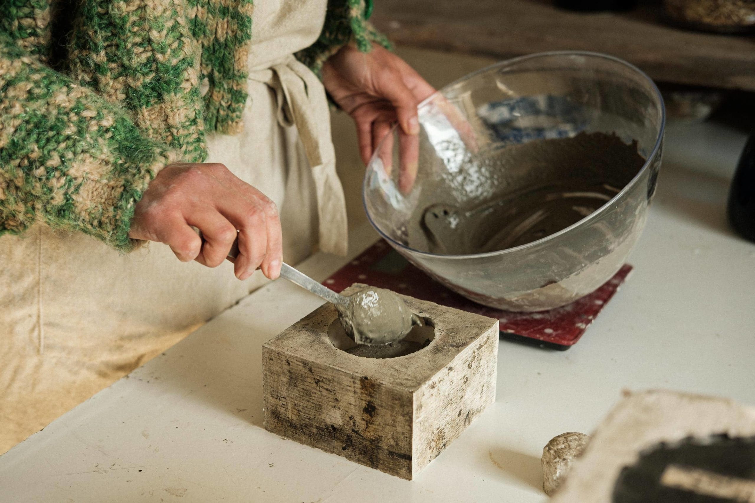 Margarida coloca cimento ainda líquido dentro de molde de gesso, com o auxílio de colher.