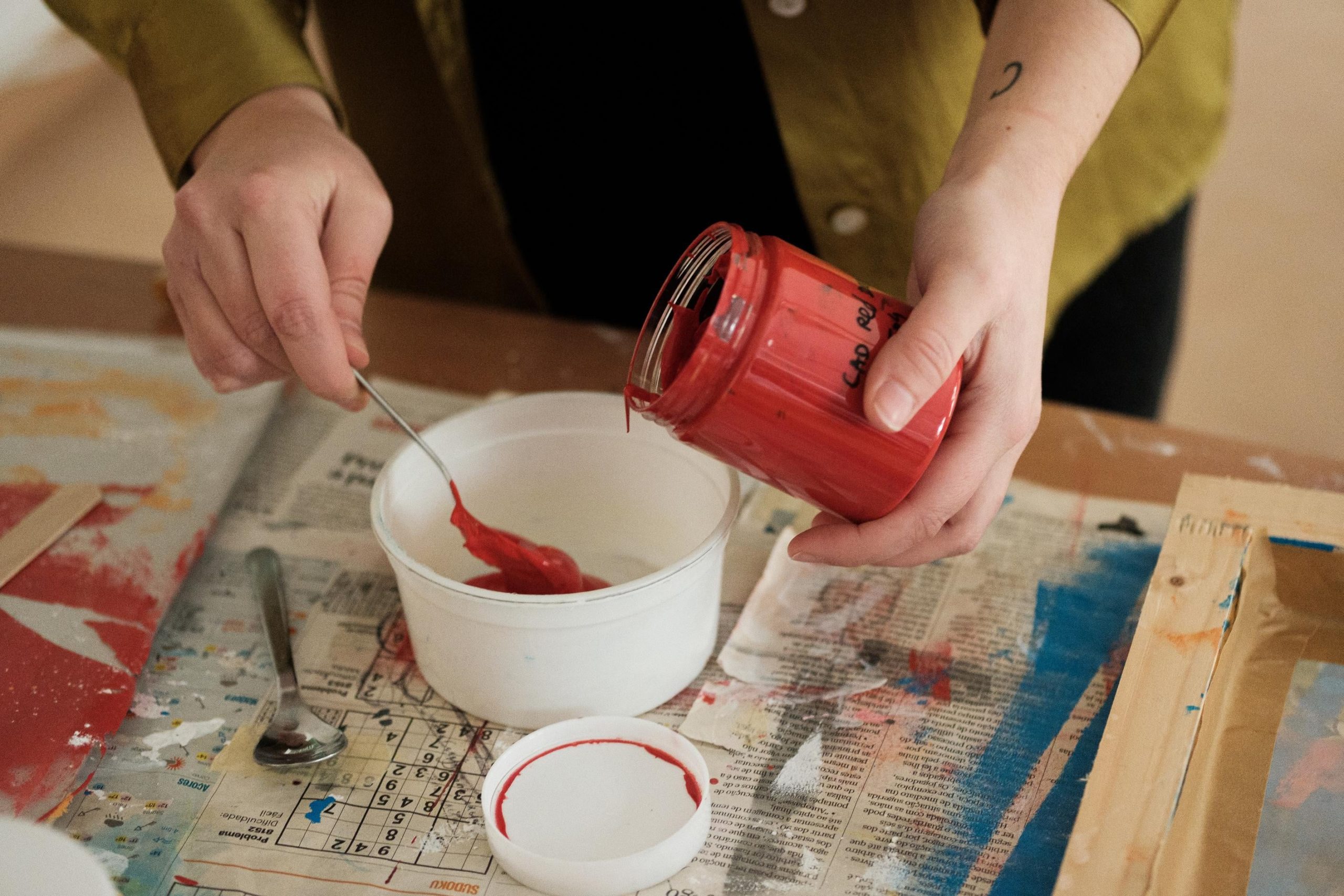 Artista verte tinta vermelha de um frasco para um recipiente com o auxilio de uma colher