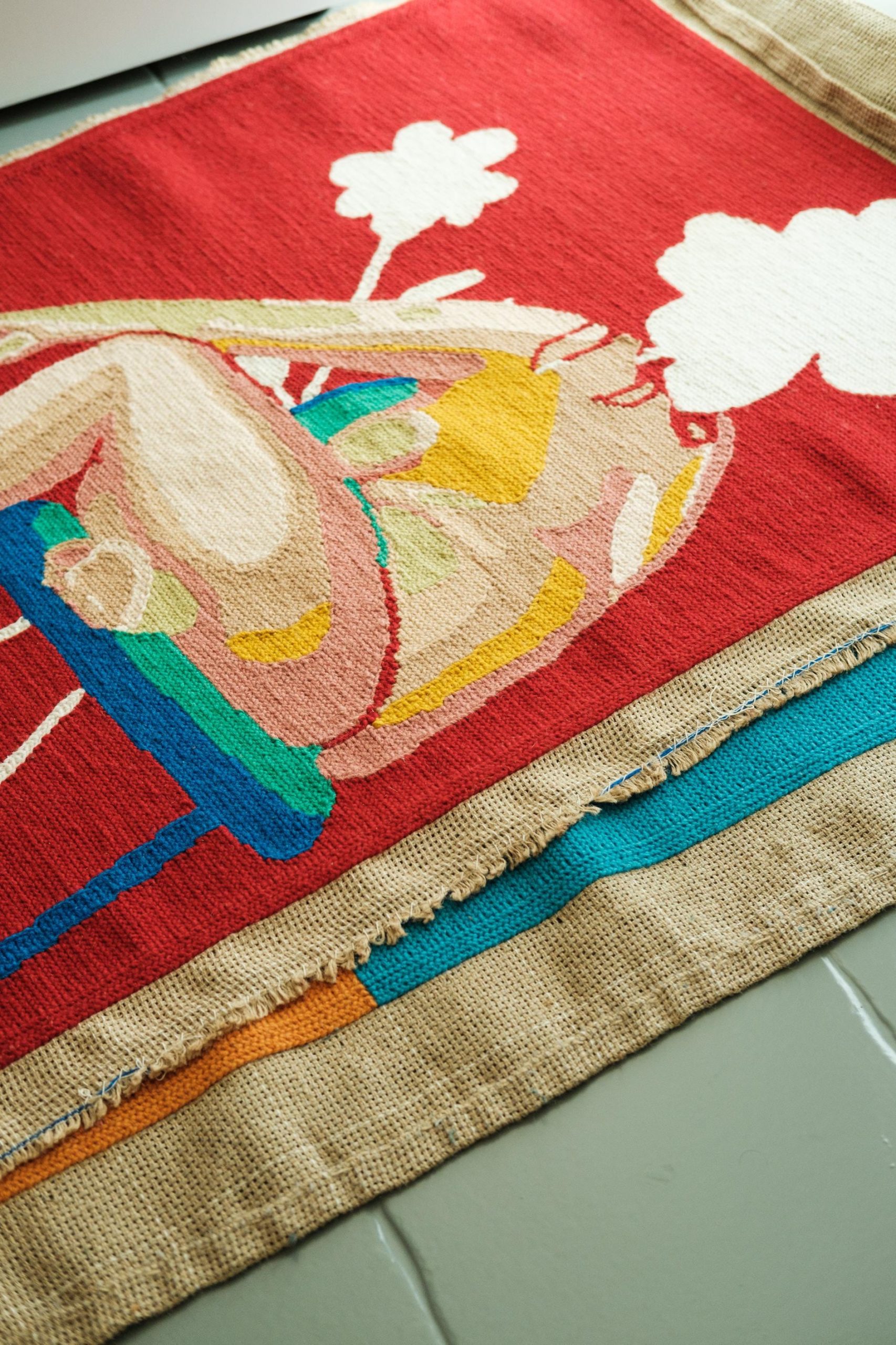 Duas tapeçarias sobrepostas ao chão. A primeira mostra um trabalho colorido do corpo de uma mulher nua, usando cores diferentes para cada detalhe e tonalidade.