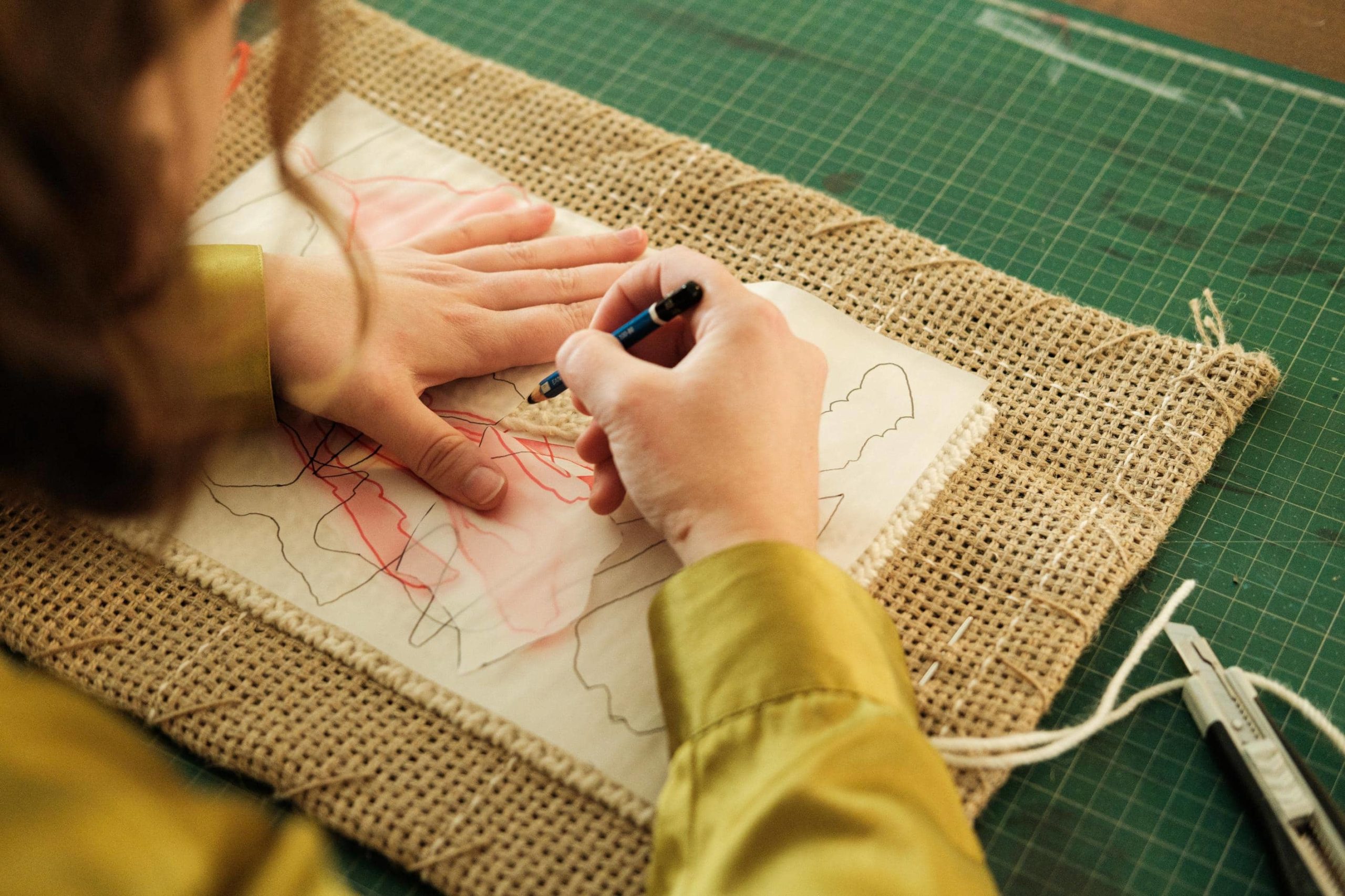 Artista transfere desenho de papel vegetal para tela de serapilheira semi-bordada.