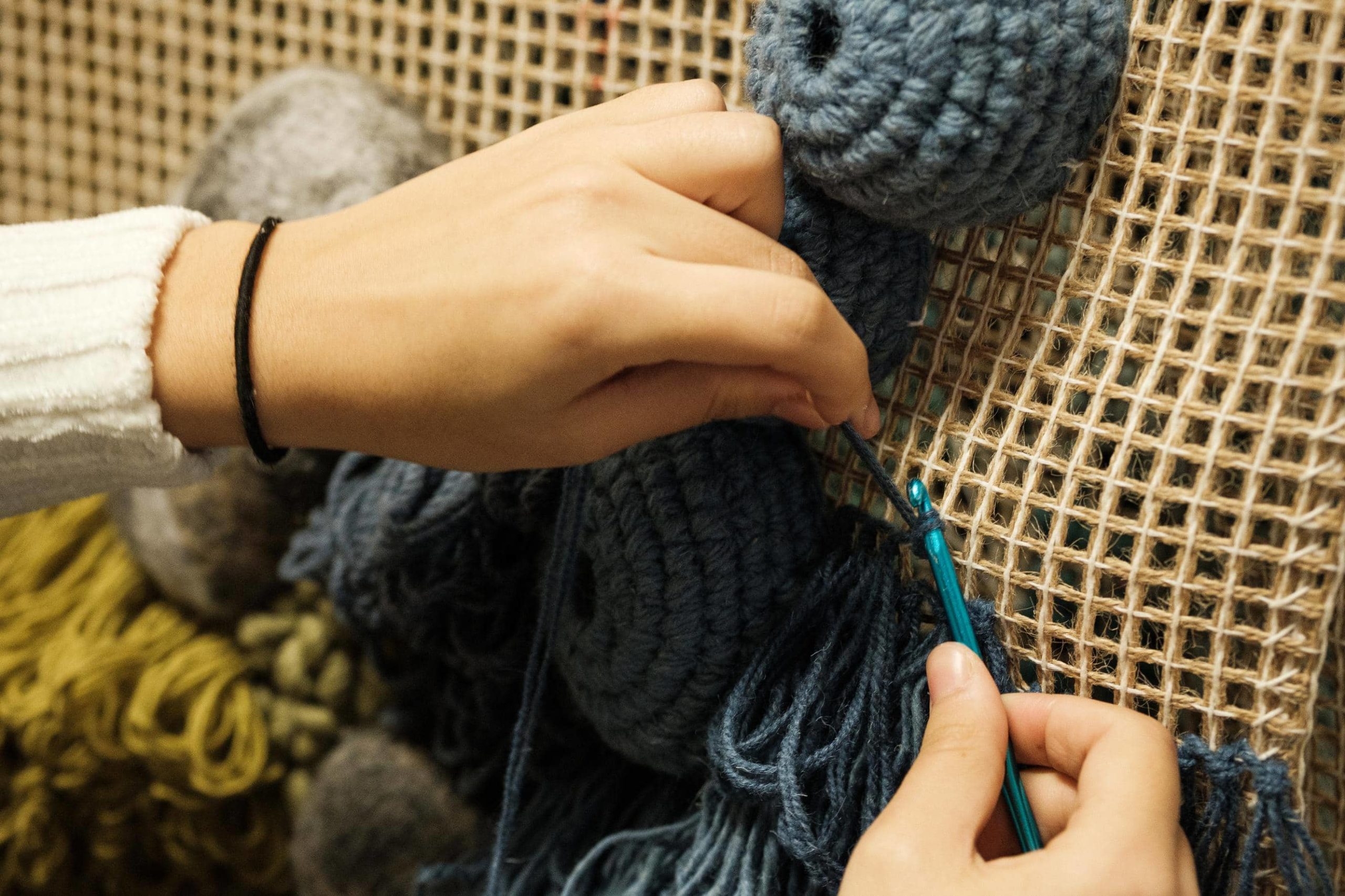 Mão do artesã costura o fio na trama com uma agulha de crochê.