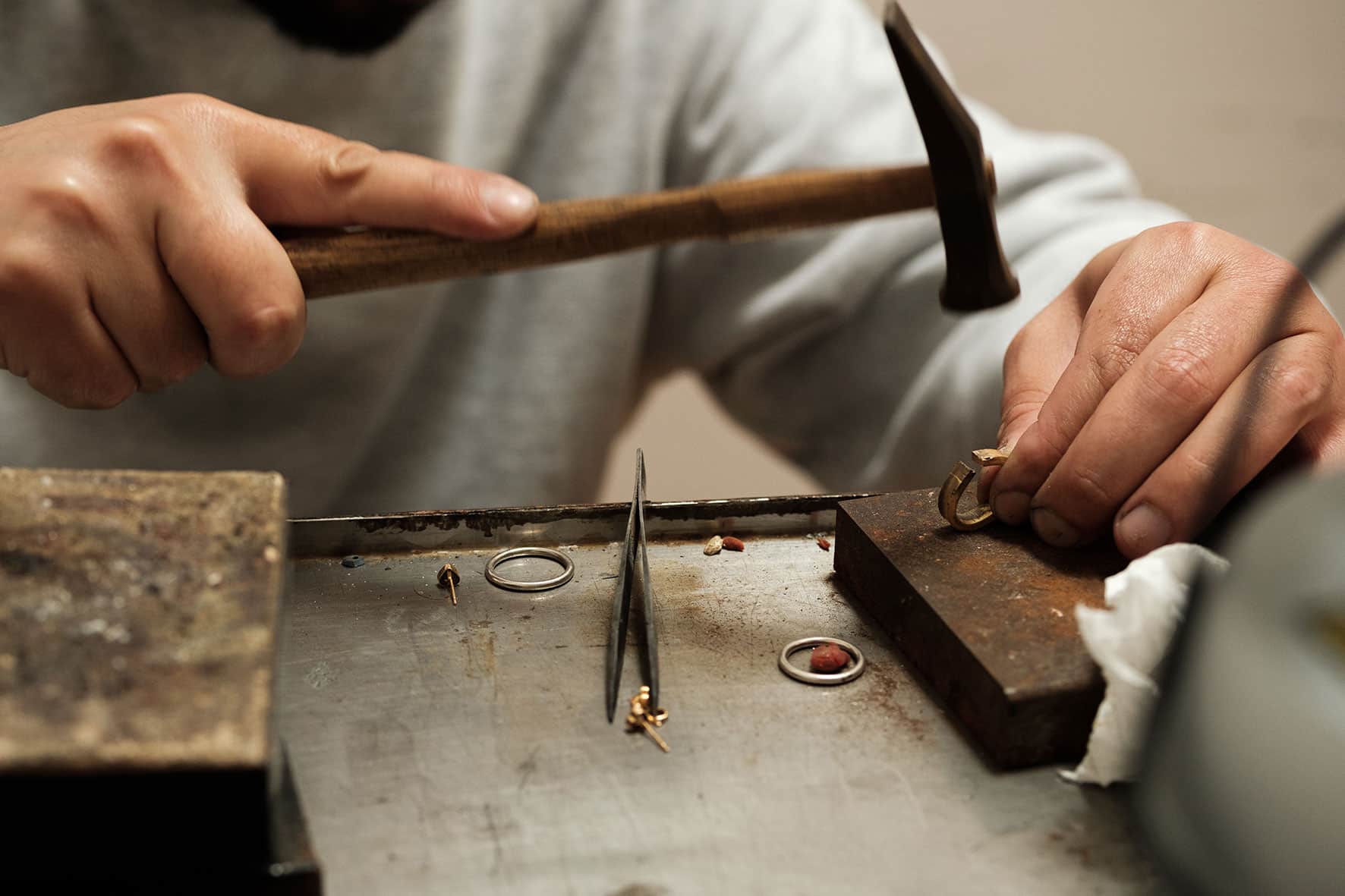 Jeweller hammers a golden ring. Tweezers, other rings on top of the bench.