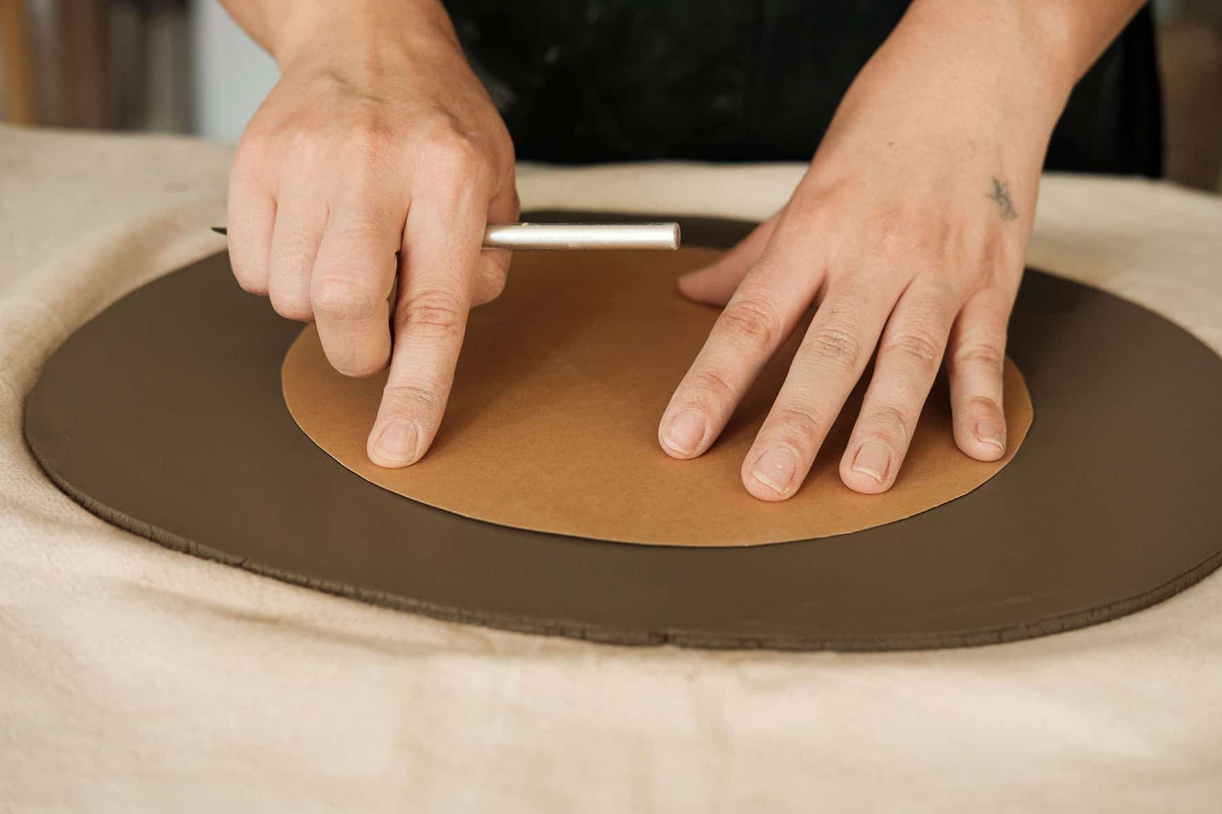 Ceramista utiliza molde circular em cima de lastra de barro.