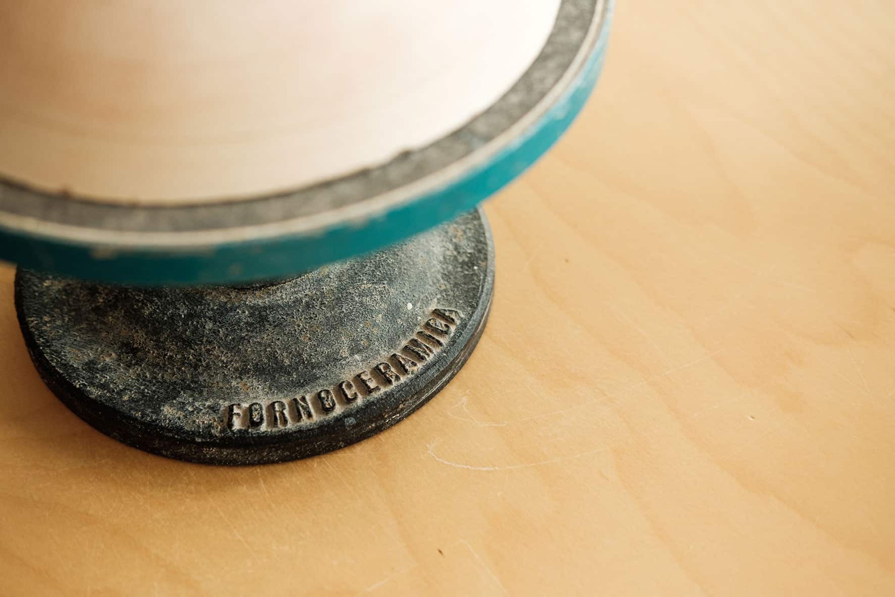 Detalhe da base de um torno de cerâmica, de arestas azuis, onde se lê em maiúsculas as palavras FORNO CERAMICA.