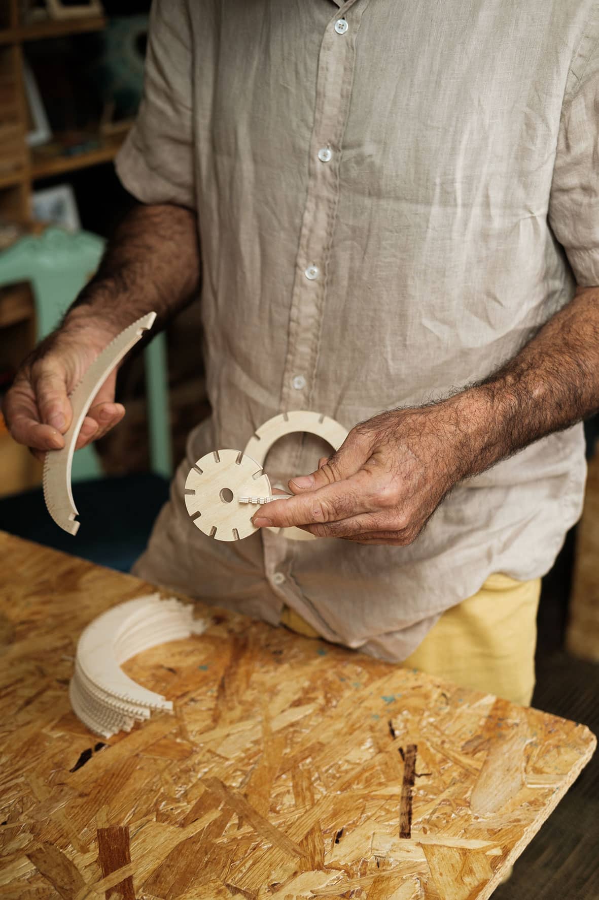 Detalhe de mãos de artesão enquanto manuseia partes de madeira de peça em construção.